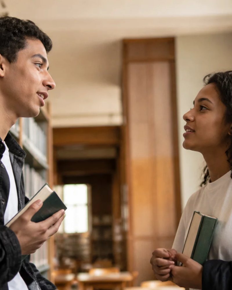 Duas participantes conversando de pé entre as prateleiras de uma biblioteca